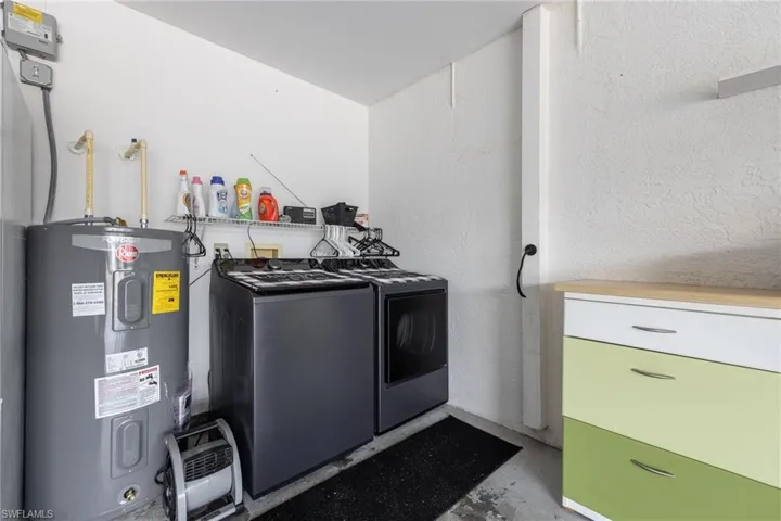 Dedicated laundry area featuring a water heater, laundry machines, and a wire storage shelf