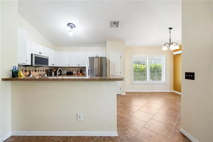 Kitchen featuring white cabinetry, stainless steel appliances, a bar-height counter, and an adjacent dining area with window shutters