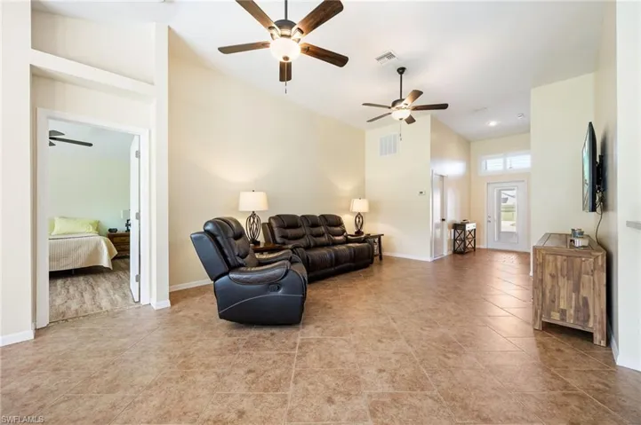 Spacious living area featuring vaulted ceilings, ceiling fans with integrated lighting, durable tile flooring, and a glass-paned entry door with transom windows