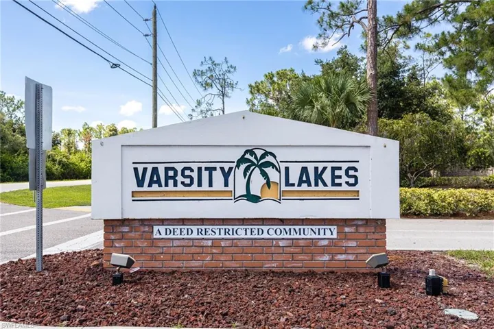 Community entrance sign for Varsity Lakes, featuring brick detailing, landscape lighting, and tropical foliage