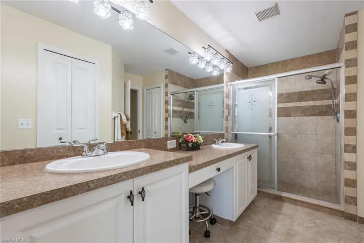 Dual vanity with integrated sinks, textured countertop, white cabinetry with decorative hardware, and a framed mirror