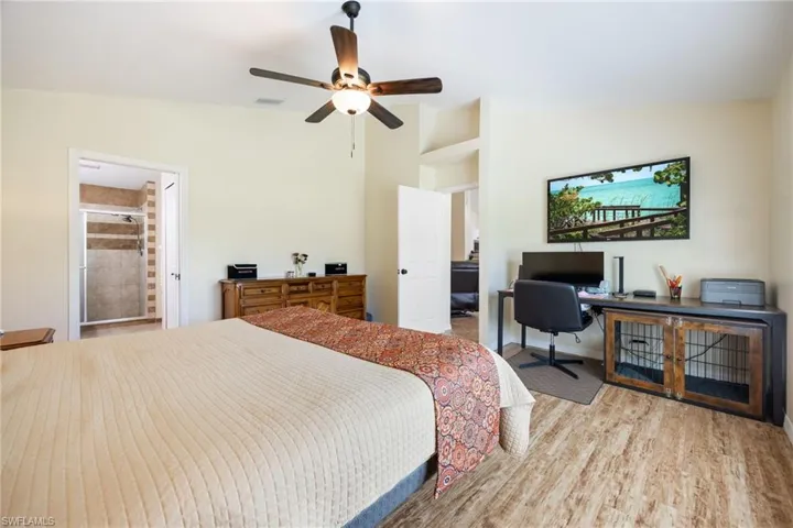 Spacious room featuring wood-finish flooring, a ceiling fan with integrated lighting, and direct access to an attached bathroom with a shower enclosure