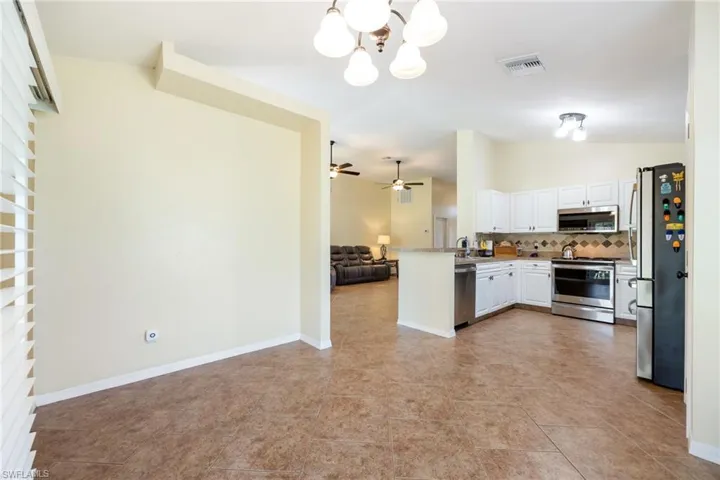 Open-concept kitchen and dining area featuring tile flooring, white cabinetry, stainless steel appliances, and an elevated breakfast bar