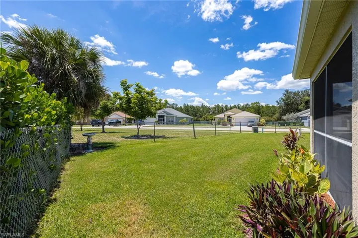 Expansive green lawn with mature landscaping, partial chain link fencing, a palm tree, and a screened enclosure visible