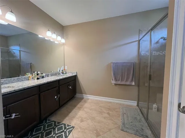Bathroom featuring a dual vanity with granite countertops, a large mirror, and a glass-enclosed shower
