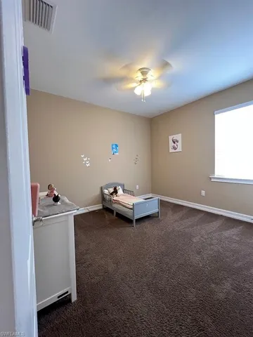 Unfurnished bedroom with dark carpet and ceiling fan