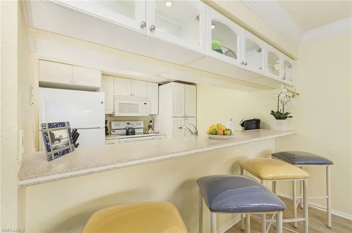 Kitchen with crown molding, a breakfast bar, light wood-type flooring, white cabinetry, and white appliances