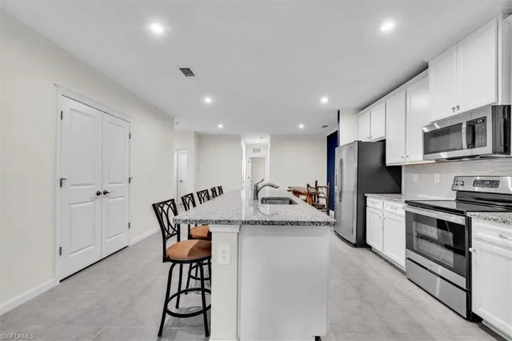 Kitchen featuring an island with stone countertop, stainless steel appliances, recessed lighting, white cabinetry, and a tile backsplash