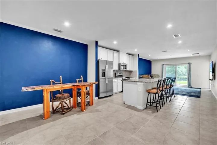 Spacious open-concept living area featuring large format tile flooring, a kitchen island with seating, white cabinetry, and stainless steel appliances