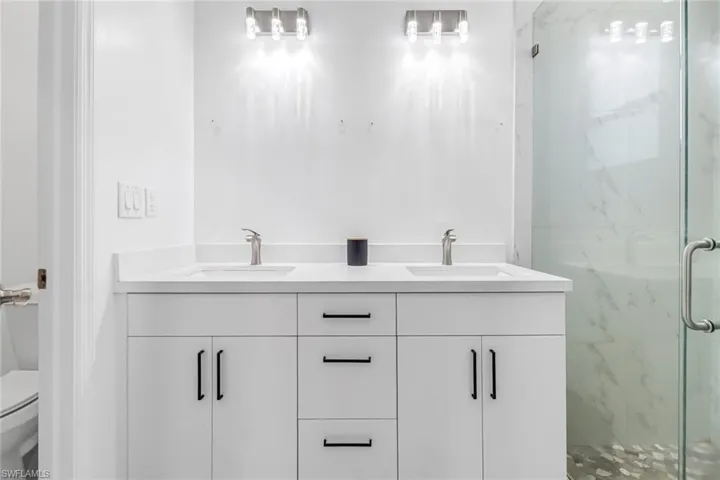 Bathroom featuring double sink vanity, a shower with shower door, and toilet