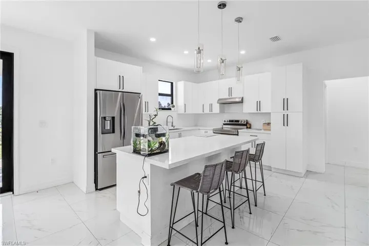 Kitchen featuring pendant lighting, appliances with stainless steel finishes, white cabinets, light tile patterned flooring, and a center island