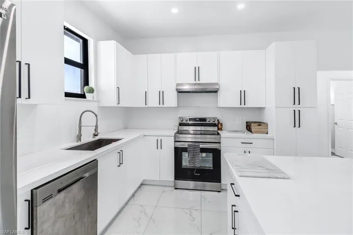 Kitchen with light tile patterned floors, white cabinets, stainless steel appliances, and sink