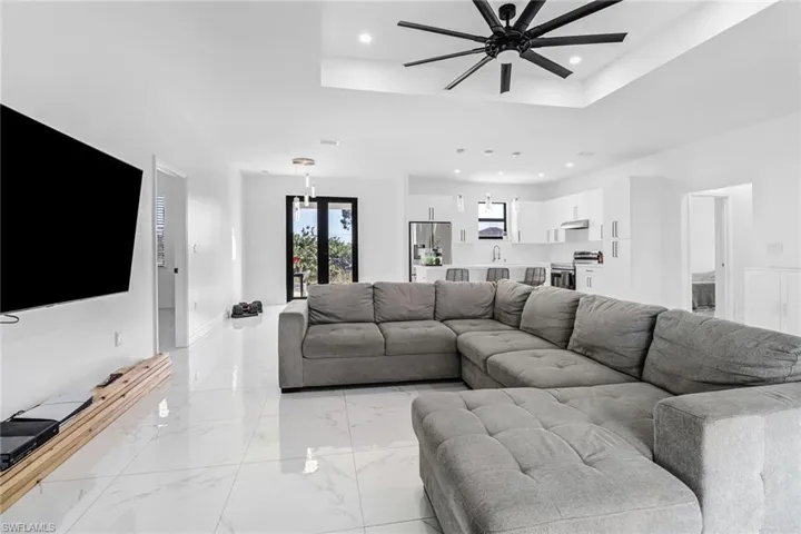 Living room with ceiling fan, a raised ceiling, sink, and light tile patterned flooring