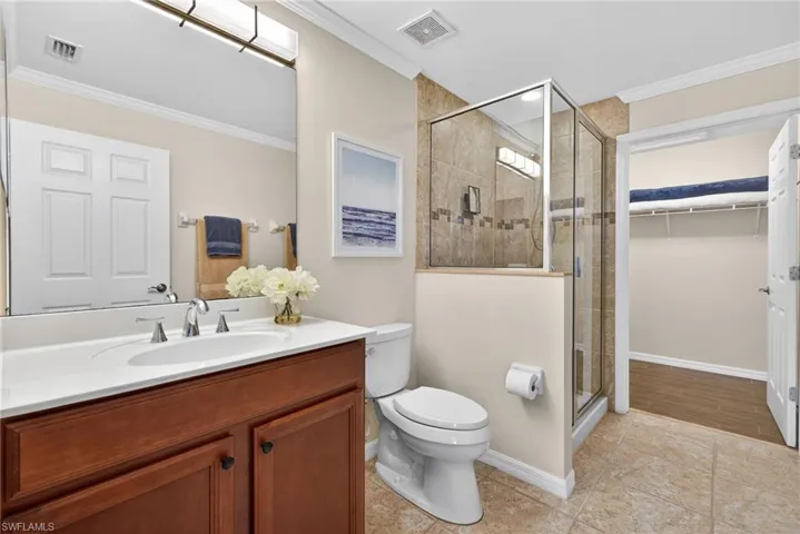 Full bathroom featuring a shower stall, crown molding, vanity, and a walk in closet