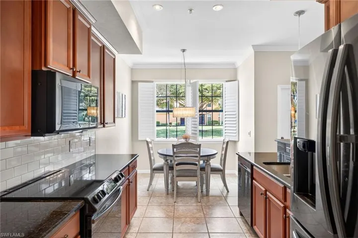 Kitchen with stainless steel appliances, wood finish cabinetry, pendant lighting, ornamental molding, and dark stone countertops