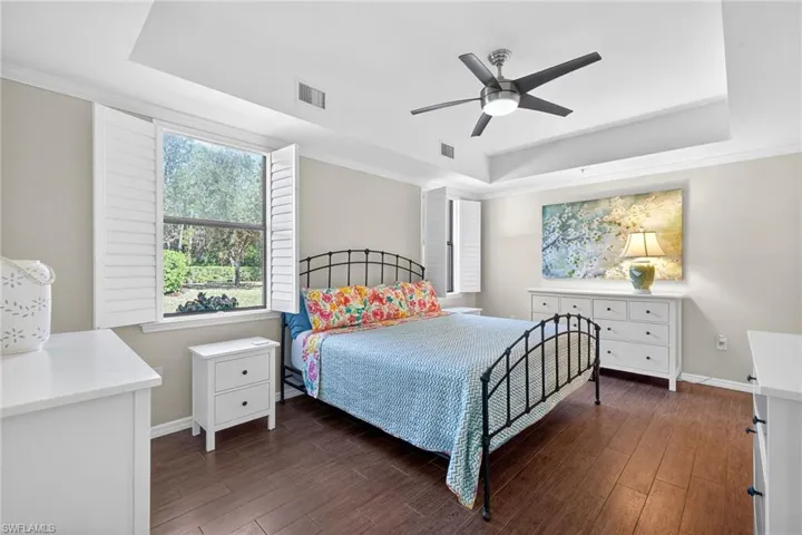 Bedroom with a raised ceiling, dark wood finished floors, a ceiling fan, and crown molding