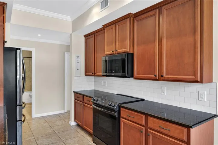 Kitchen with black appliances, crown molding, decorative backsplash, dark stone counters, and wood finish cabinets