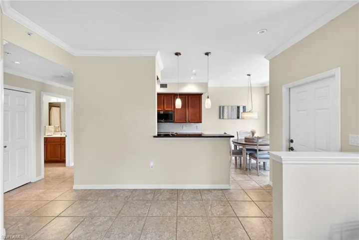 Kitchen with dark countertops, hanging light fixtures, crown molding, backsplash, and stainless steel microwave