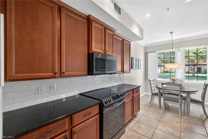 Kitchen featuring ornamental molding, black / electric stove, stainless steel microwave, dark stone countertops, and tasteful backsplash