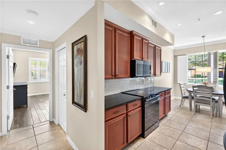 Kitchen featuring black range with electric stovetop, ornamental molding, light tile patterned flooring, stainless steel microwave, and decorative backsplash