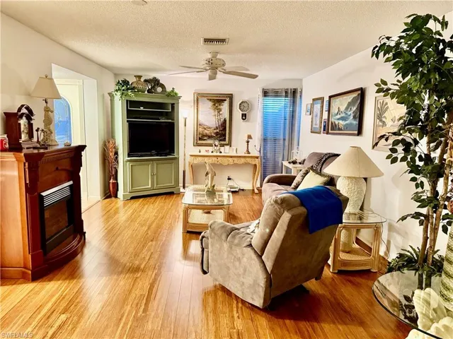 Living area featuring light wood-style flooring, a textured ceiling, a fireplace, and ceiling fan