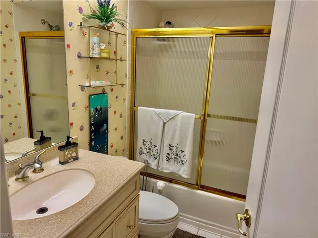 Full bath with vanity, combined bath / shower with glass door, and wallpapered walls