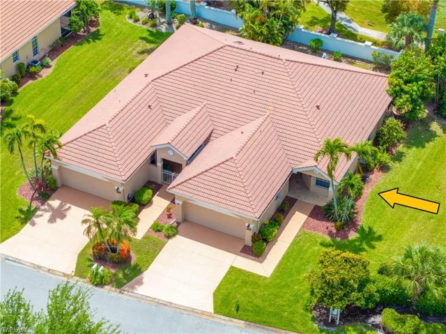 The property features a terracotta tile roof, well-maintained lawn, multiple palm trees, and two separate driveways leading to garages
