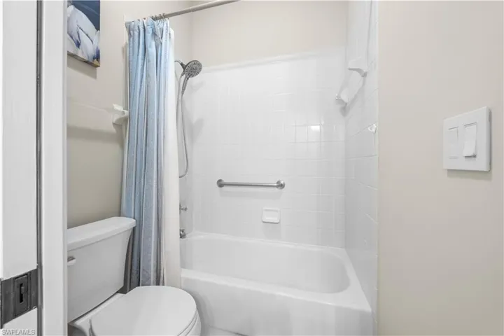 Bathroom featuring a bathtub with white tiled walls and a shower fixture, a white toilet, and a grab bar