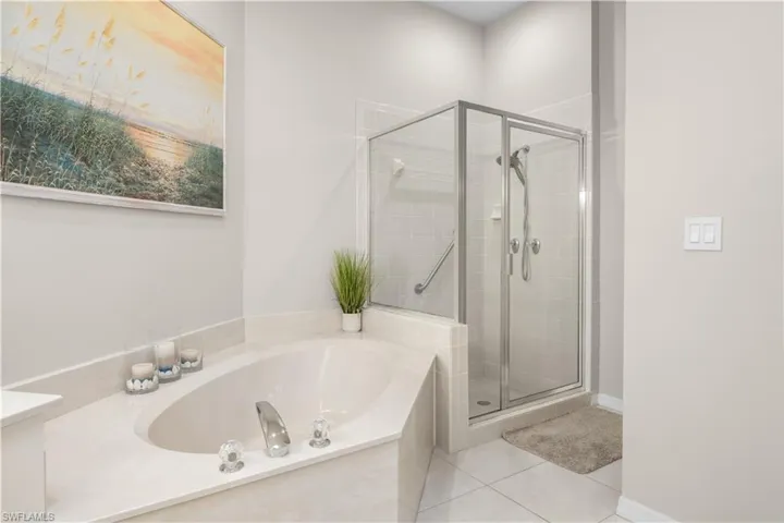 Bathroom featuring a built-in bathtub with polished chrome fixtures, a glass-enclosed shower with a tiled surround, and light-colored tiled flooring