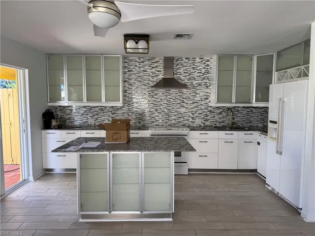 Kitchen prior to changing light fixtures and adding bar stools etc.  it features white appliances, a sink, wall chimney range hood, backsplash, and wood tiled floor