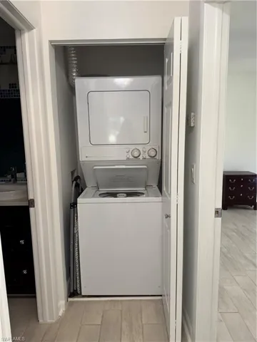 Clothes washing area with stacked washer and dryer, wood tiled floor, and a sink