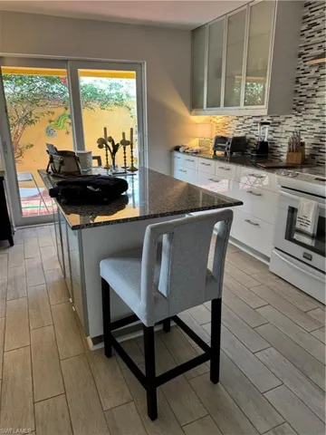 Kitchen with wood tiled floors, stove, dark stone counters, backsplash, and a center island