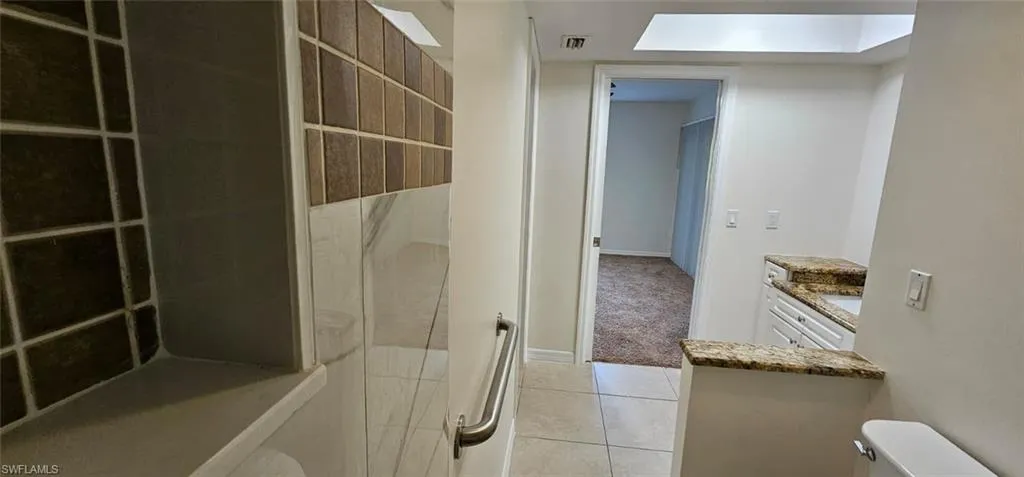 Full bathroom with vanity, light tile patterned flooring, a tile shower, and a skylight