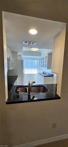 Kitchen with dark stone countertops, white cabinetry, white appliances, and recessed lighting