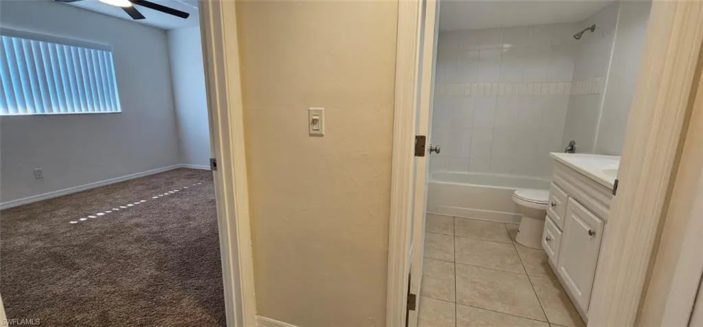 Guest Bedroom with Bathroom with vanity, shower / bathtub combination, light tile patterned flooring, light carpet, and a ceiling fan
