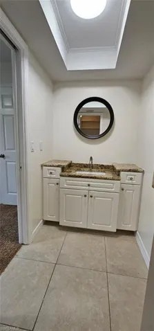 Bathroom with vanity, ornamental molding, a tray ceiling, and light tile patterned floors