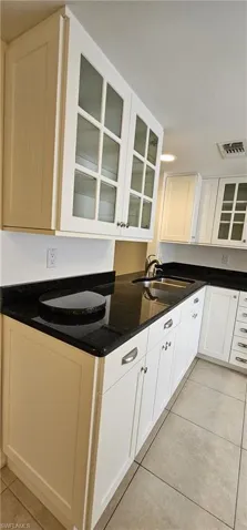 Kitchen with glass insert cabinets, white cabinetry, light tile patterned floors, and dark stone counters