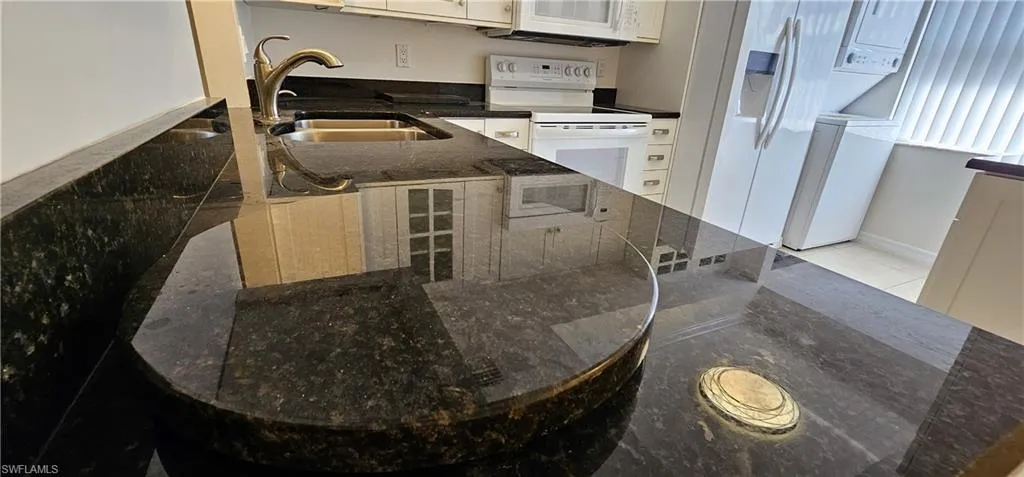 Kitchen with white appliances, dark stone countertops, and stacked washer and clothes dryer