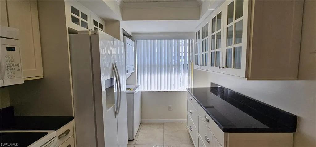 Kitchen featuring glass insert cabinets, fridge with ice dispenser, white cabinetry, and ornamental molding