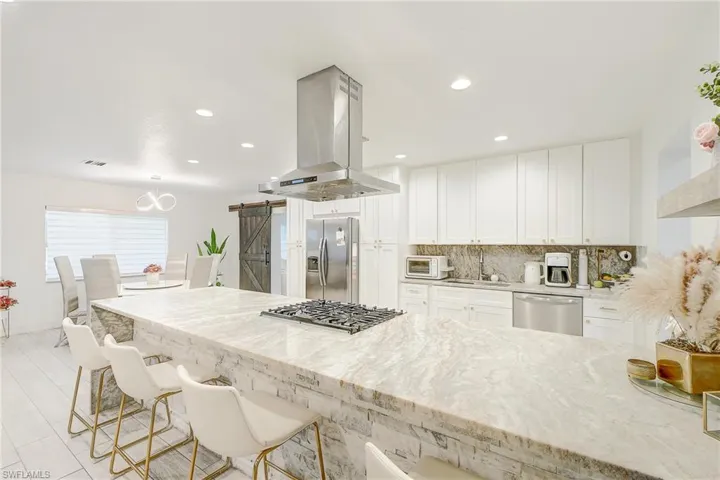 Kitchen with light stone countertops, a barn door, white cabinets, island exhaust hood, and recessed lighting