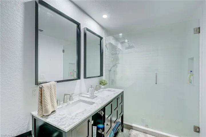 Full bathroom with a shower stall, double vanity, a textured wall, and a textured ceiling