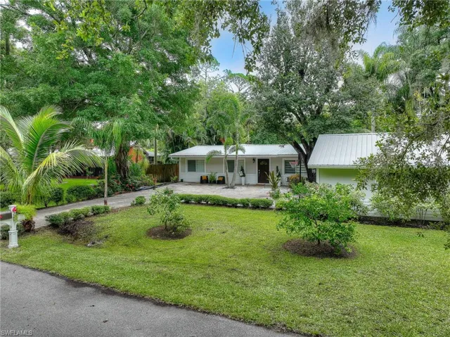 View of front of home with driveway, a metal roof, view of scattered trees, and covered porch