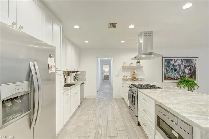 Kitchen with stainless steel appliances, white cabinets, a peninsula, recessed lighting, and island exhaust hood