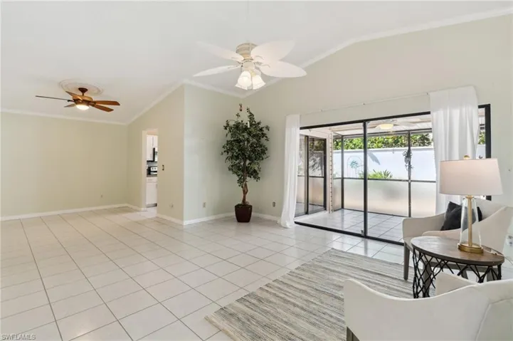 Tiled living room featuring ceiling fan, ornamental molding, and vaulted ceiling