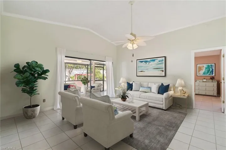 virtually staged Living area with light tile patterned flooring, vaulted ceiling, ceiling fan, ornamental molding, and baseboards