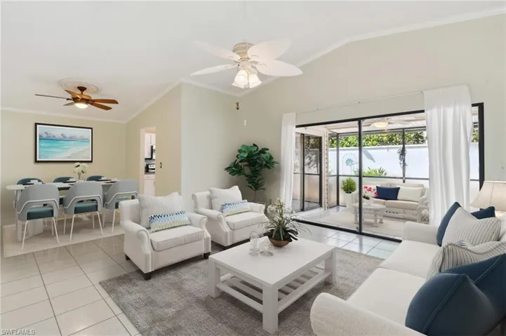 Virtually staged Living room featuring lofted ceiling, light tile patterned flooring, a ceiling fan, ornamental molding, and baseboards