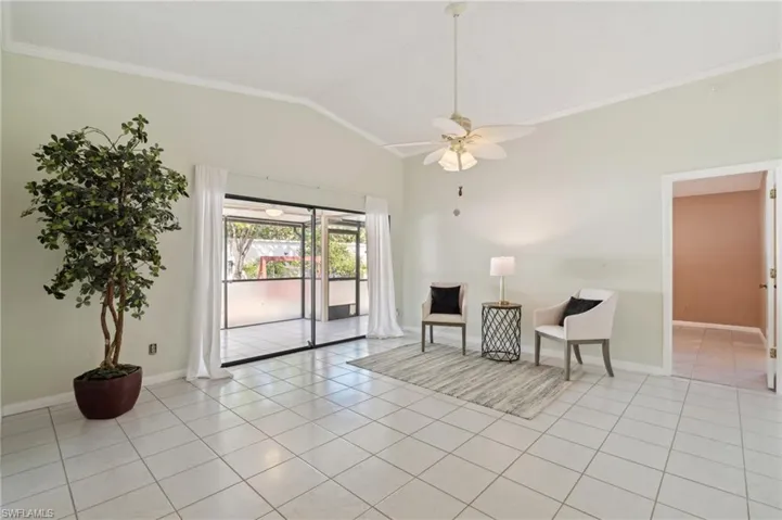 Living area with light tile patterned flooring, ceiling fan, lofted ceiling, and crown molding