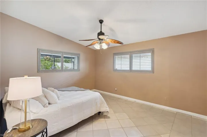 Bedroom with multiple windows, light tile patterned floors, lofted ceiling, and ceiling fan