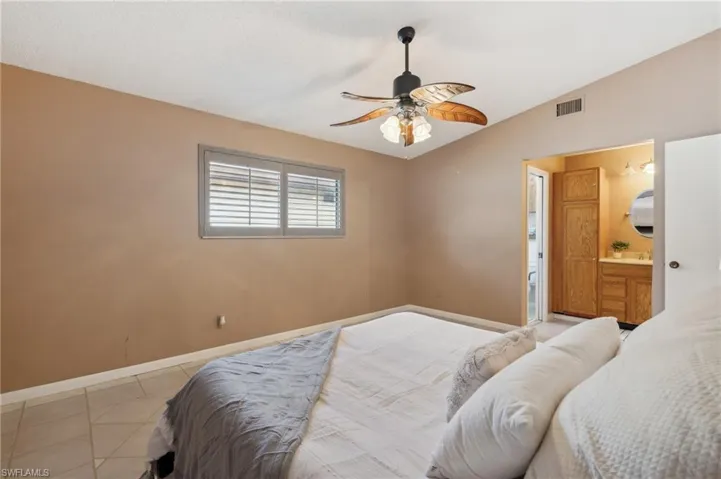 Bedroom featuring lofted ceiling, light tile patterned floors, ceiling fan, and ensuite bath