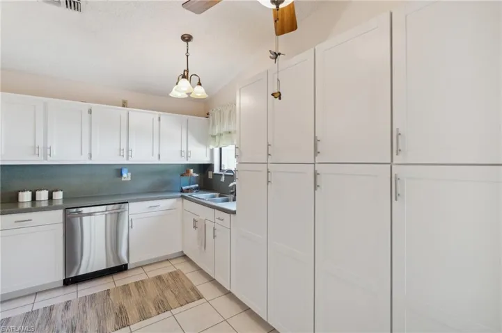 Kitchen featuring sink, light tile patterned floors, dishwasher, ceiling fan, and white cabinetry